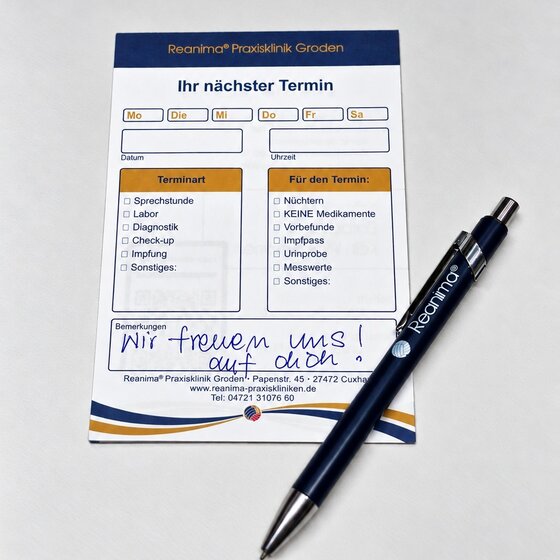 Ein Terminkarten-Format der Reanimra® Praxis, auf dem der nächste Termin festgehalten werden kann. Es gibt Kästchen für Daten und Uhrzeiten sowie Platz für Notizen. Neben der Karte liegt ein blauer Stift mit dem Namen der Praxis.